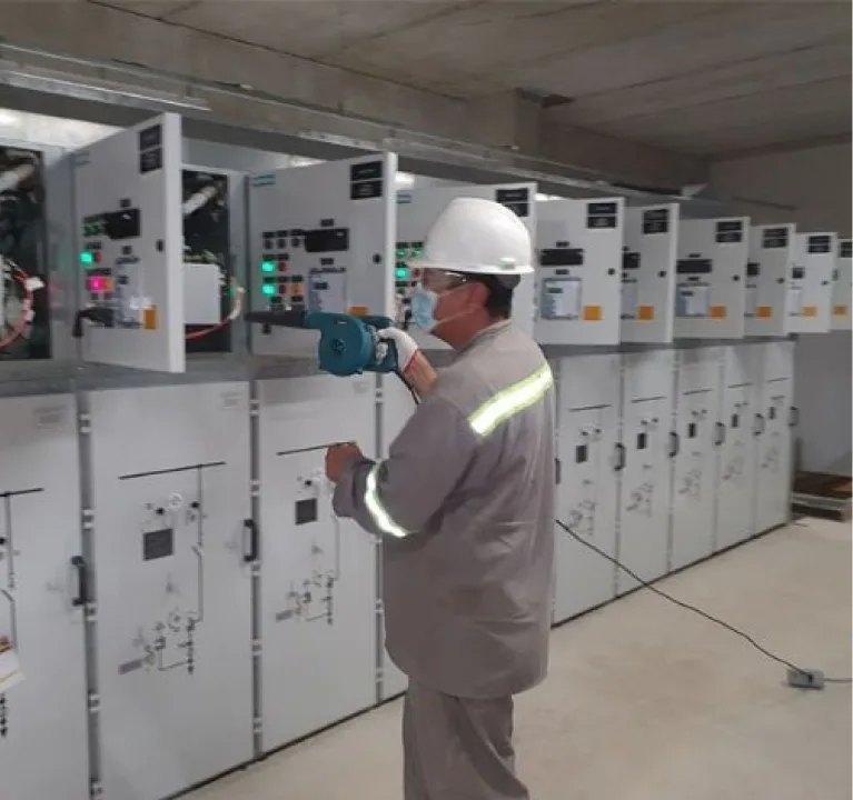 Técnico de capacete e uniforme cinza operando um painel de média tensão