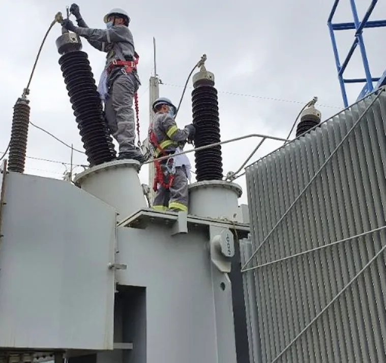 Técnicos com equipamento de proteção sobre um transformador de subestação
