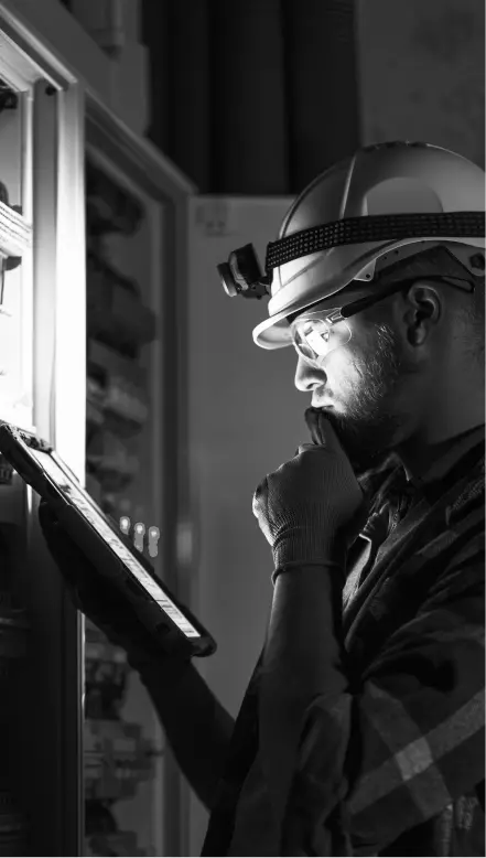 Eletricista de capacete com lanterna inspecionando um painel elétrico